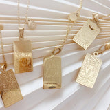 Gold tarot card pendants on a textured white surface