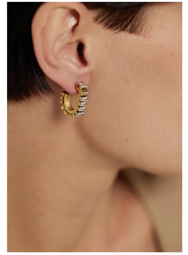 Gold hoop earring with gemstone worn by a person on a white background.