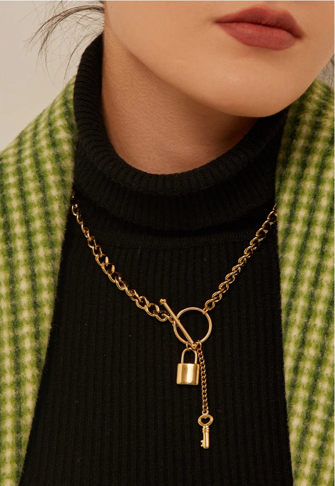 Gold necklace with lock and key pendant worn by a person in a green checkered jacket.