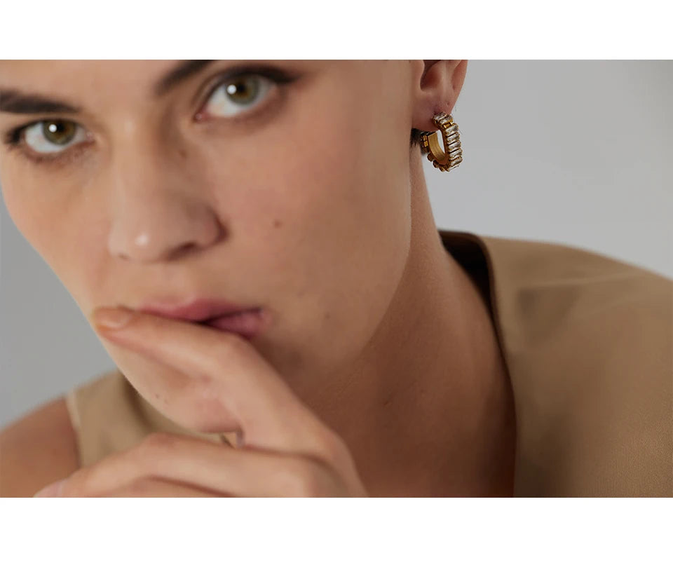 Close-up of a person wearing gold hoop earrings with a neutral background
