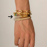 Hand wearing multiple gold and pearl bracelets on a neutral background
