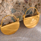Gold earrings on a textured surface with a neutral background