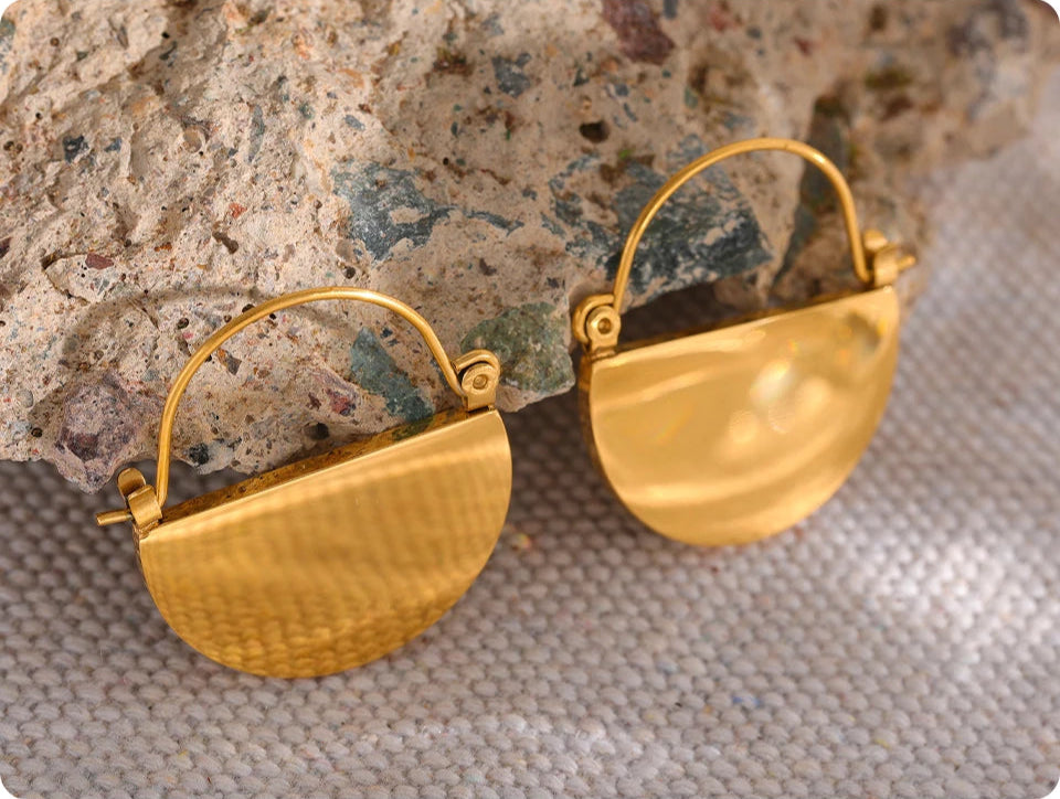 Gold earrings on a textured surface with a neutral background