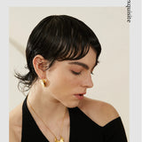 Woman wearing gold earrings and a necklace with a neutral background