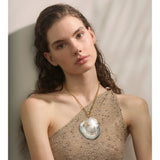 Woman wearing a gold necklace with a large shell pendant against a neutral background