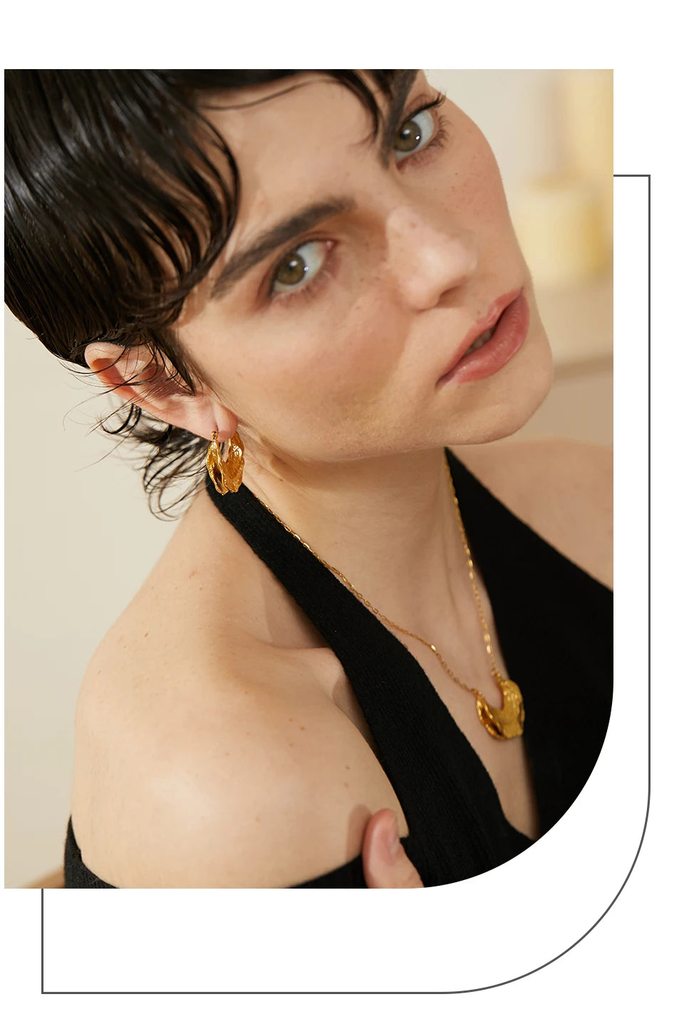 Woman wearing gold earrings and a necklace against a neutral background