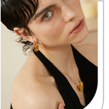Woman wearing gold earrings and a necklace against a neutral background