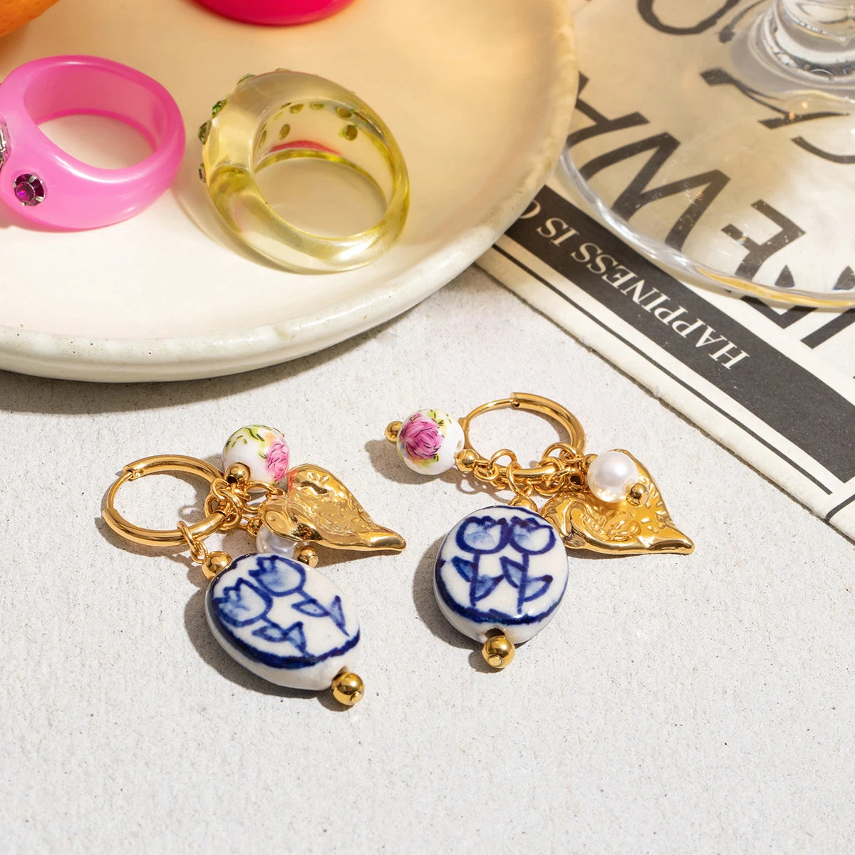 Pair of earrings with blue and white designs on a surface with a magazine underneath