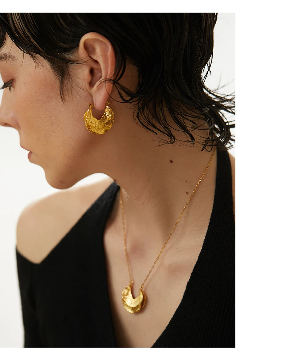 Close-up of a person wearing gold earrings and a necklace with a plain background