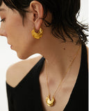 Close-up of a person wearing gold earrings and a necklace with a plain background