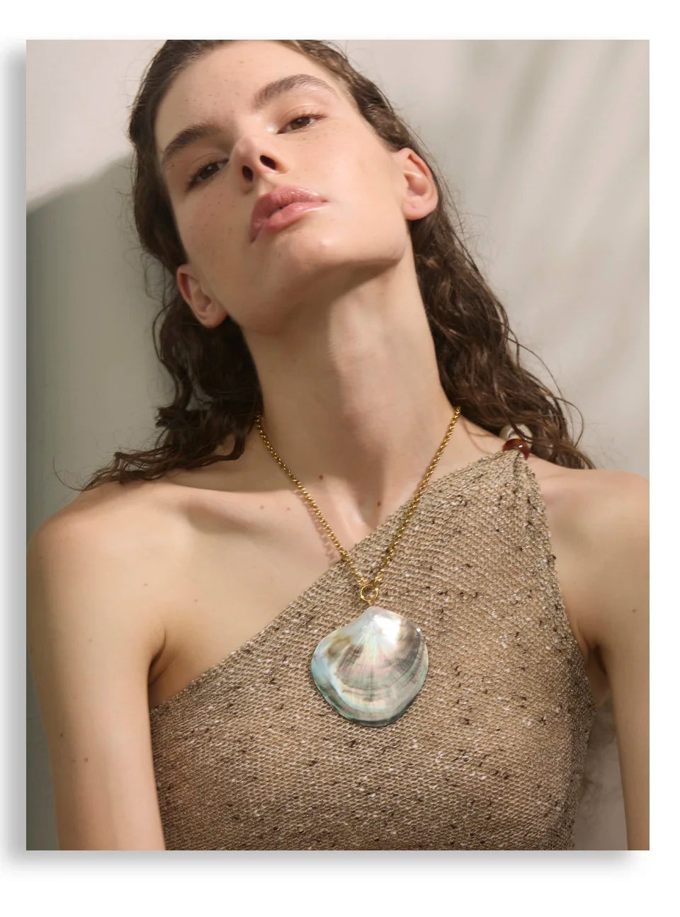 Woman wearing a gold necklace with a large pendant against a neutral background
