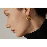 Close-up of a person wearing a gold hoop earring against a neutral background