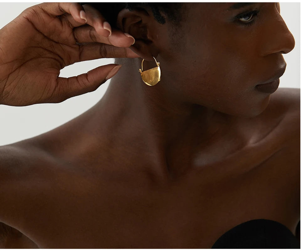 Gold earring being worn by a person with a neutral background