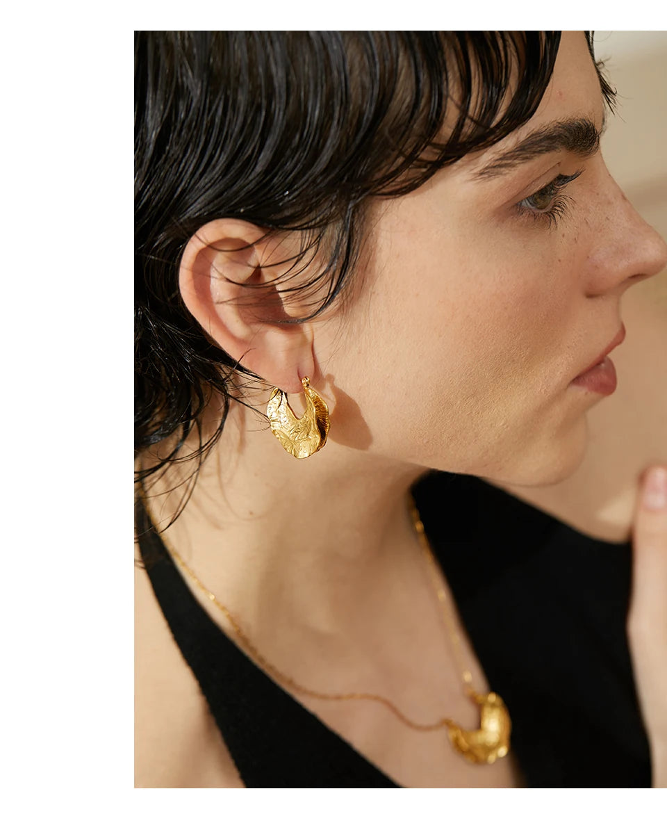 Close-up of a person wearing gold earrings and a necklace against a neutral background