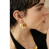 Close-up of a person wearing gold earrings and a necklace against a neutral background