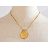Gold necklace with a round pendant on a mannequin bust.