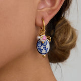 Close-up of an ear wearing a decorative earring with a blue floral design.