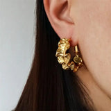 Sculptural gold ripple hoop earrings with 18k gold plating, offering a bold, modern twist on classic hoop jewelry.
