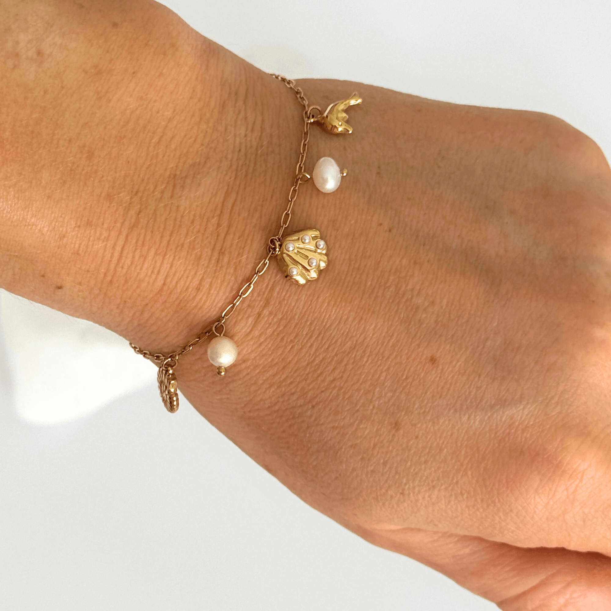 Gold sea-inspired pearl bracelet with dolphin and shell charms, perfect for ocean lovers and everyday coastal style.