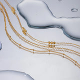 18K Gold Beaded Layered Necklace with three delicate chains and polished beads, designed to add depth and elegance to any outfit.