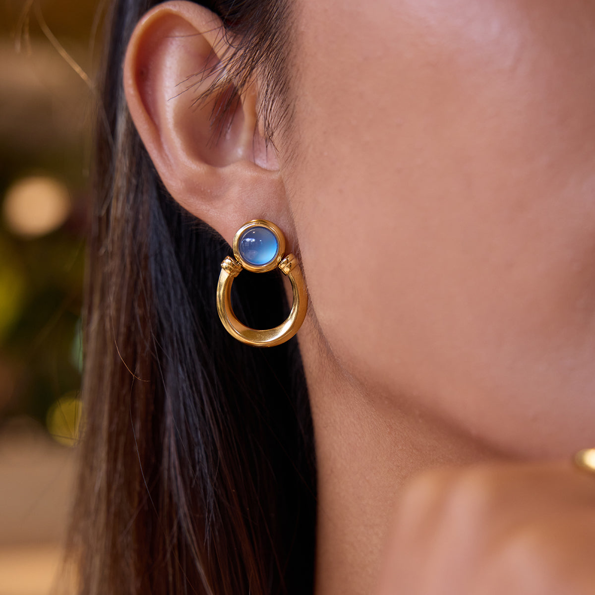 Gold earring with a blue gemstone worn by a person with dark hair.