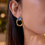 Gold earring with a blue gemstone worn by a person with dark hair.