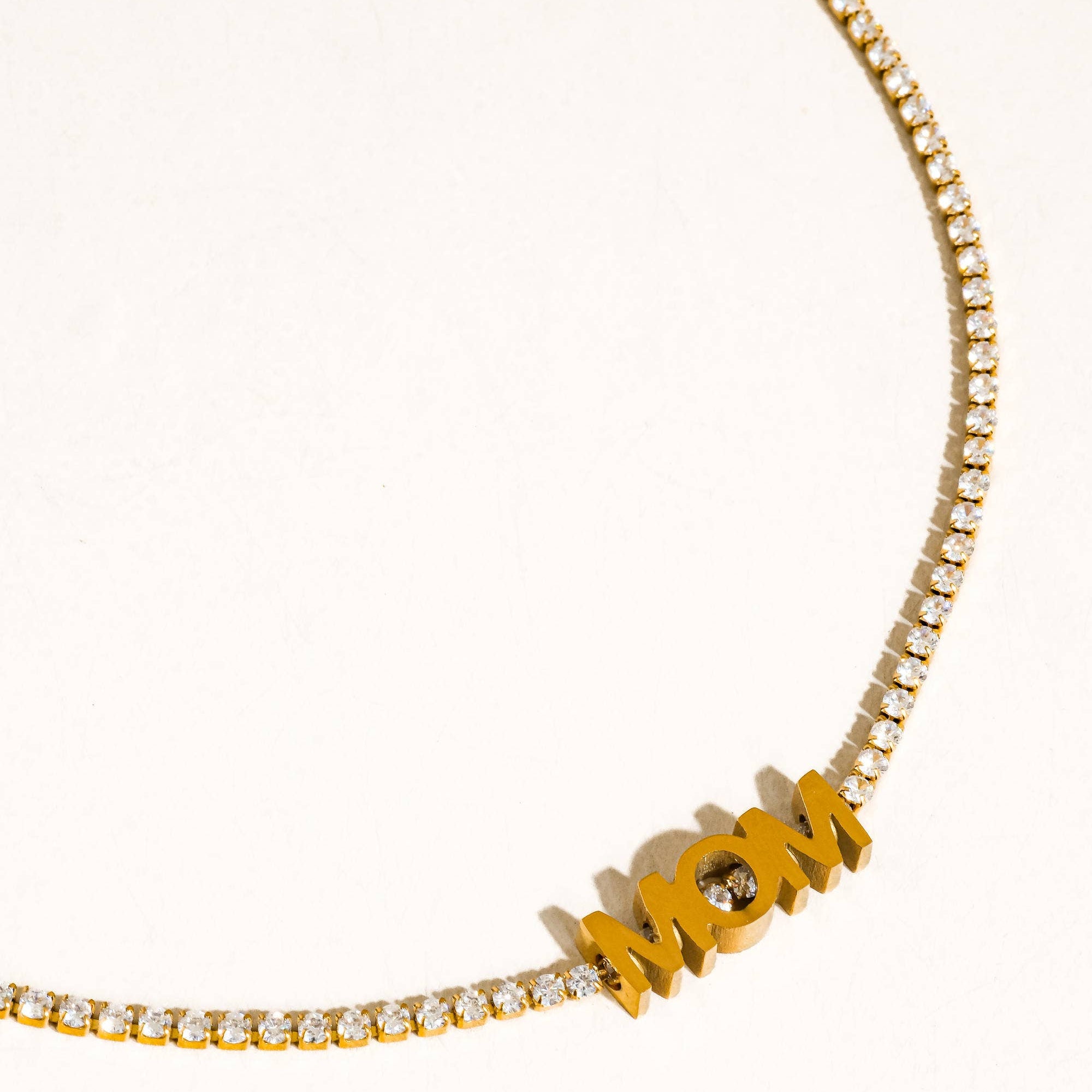 Gold necklace with 'MOM' pendant on a white background