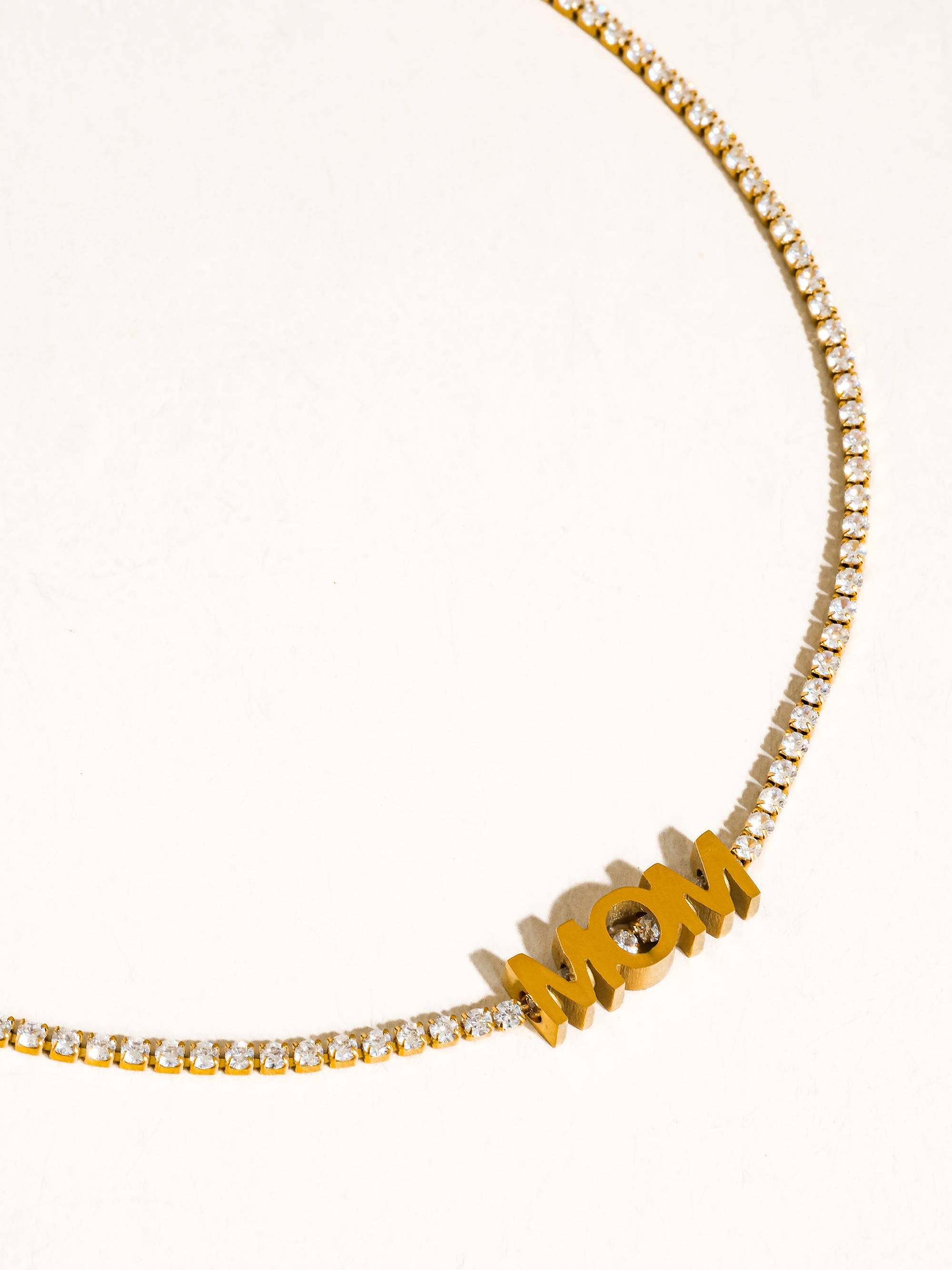 Gold necklace with 'MOM' pendant on a white background