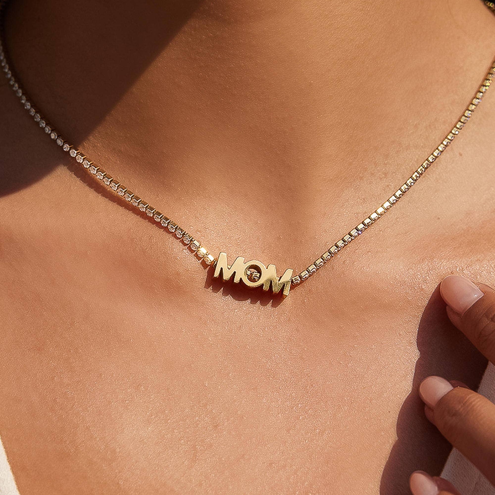Gold necklace with 'MOM' pendant on a person's neck