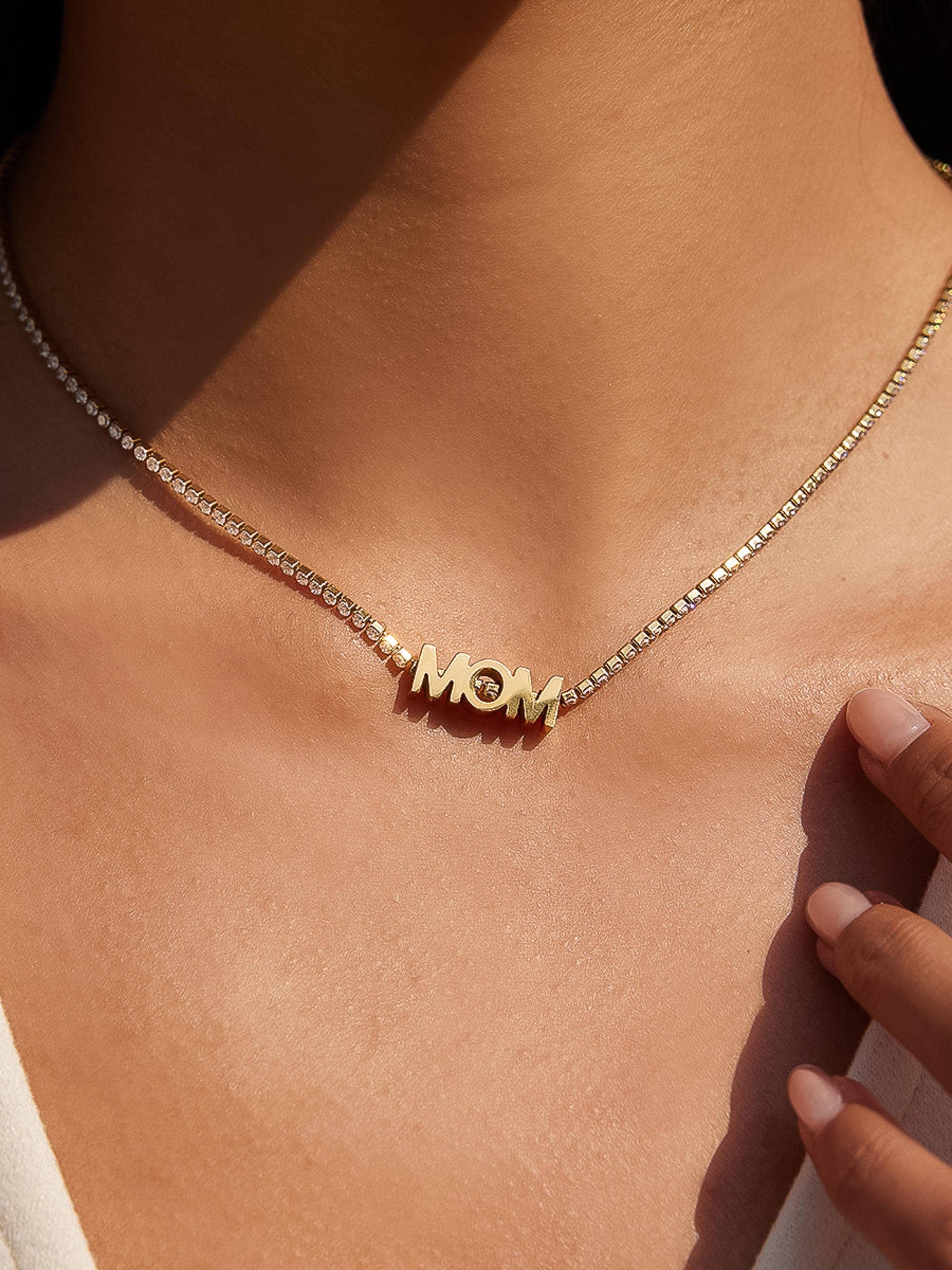 Gold necklace with 'MOM' pendant on a person's neck
