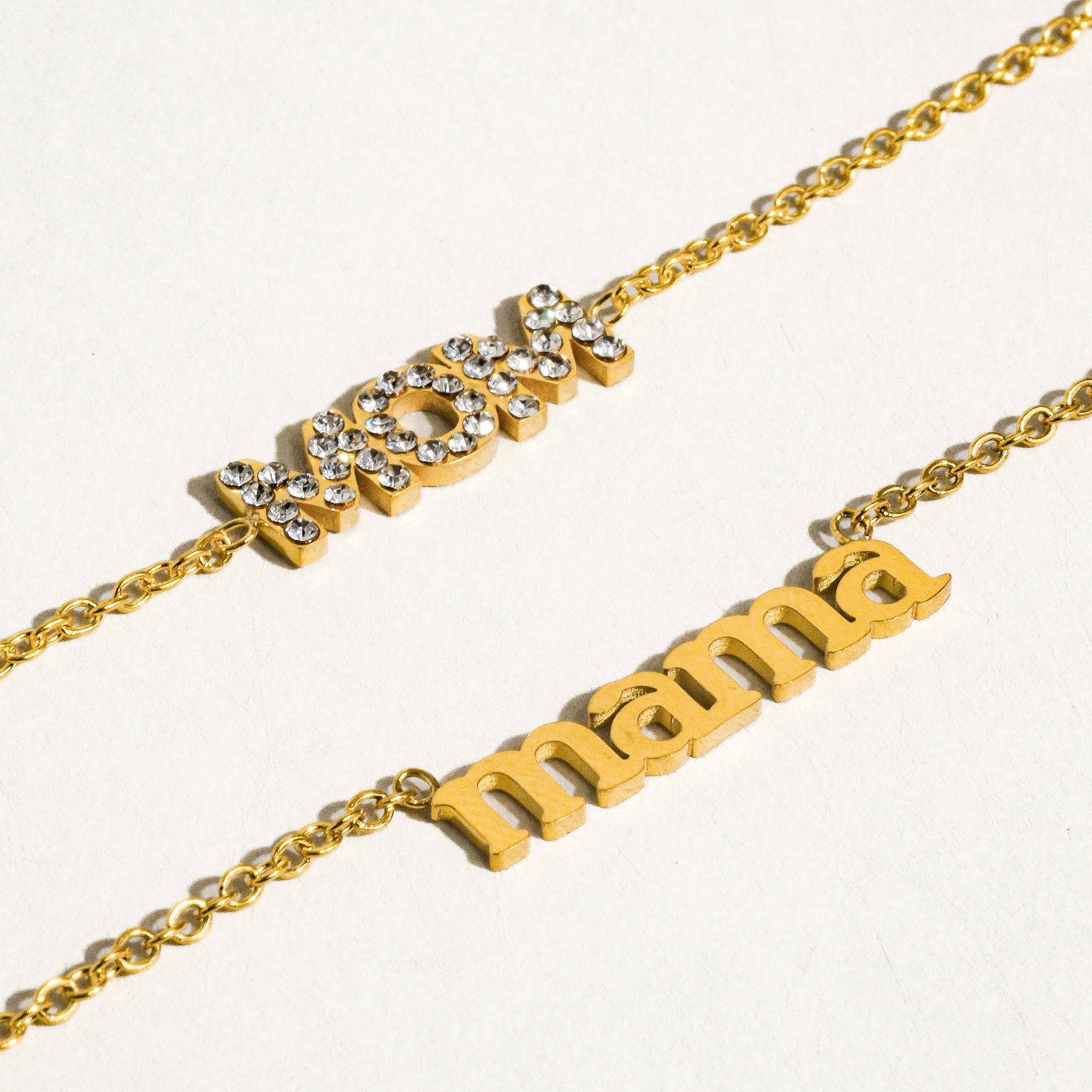 Two gold necklaces with 'mom' and 'mama' on a white background