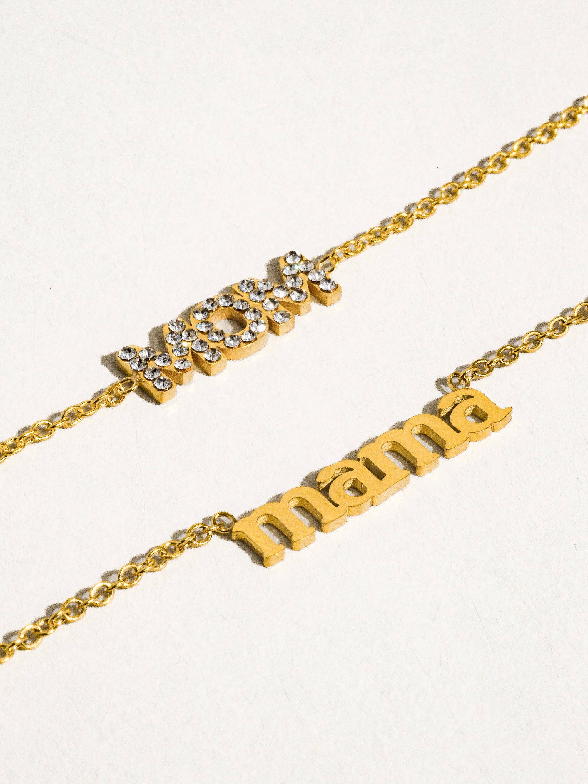 Two gold necklaces with 'mom' and 'mama' on a white background