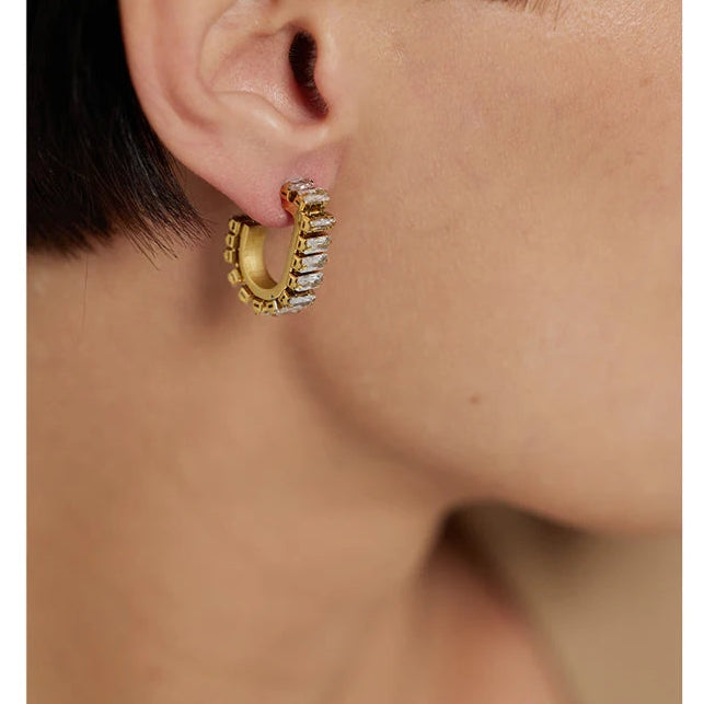 Gold hoop earring with gemstone worn by a person on a white background.