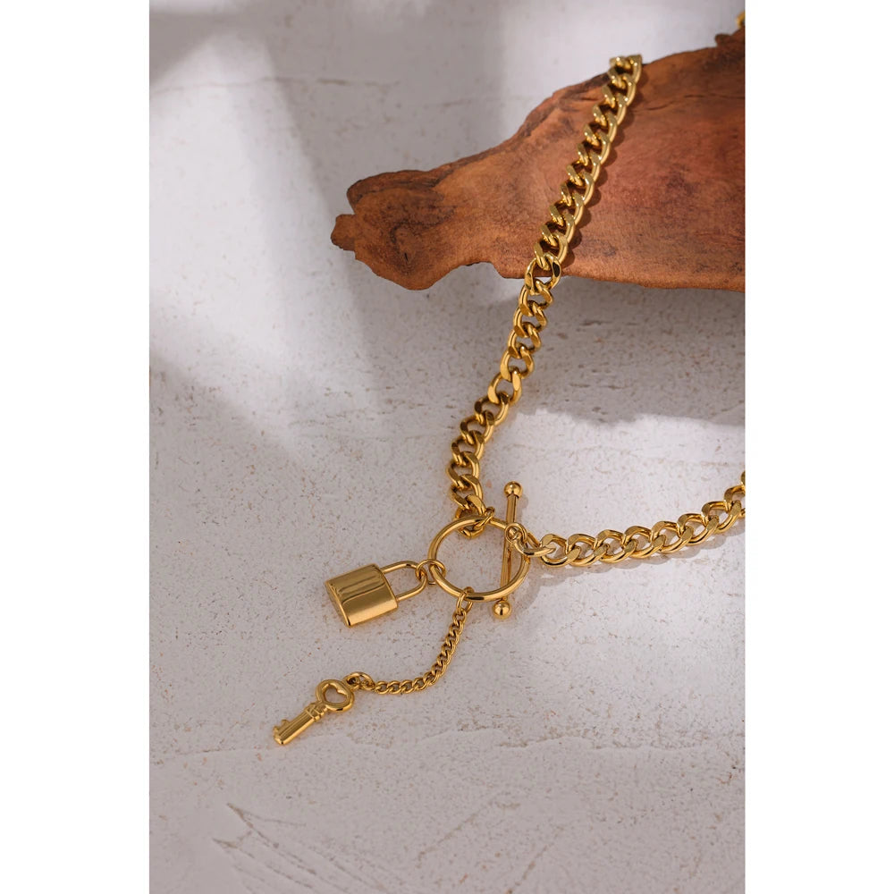 Gold chain bracelet with lock and key charms on a textured surface