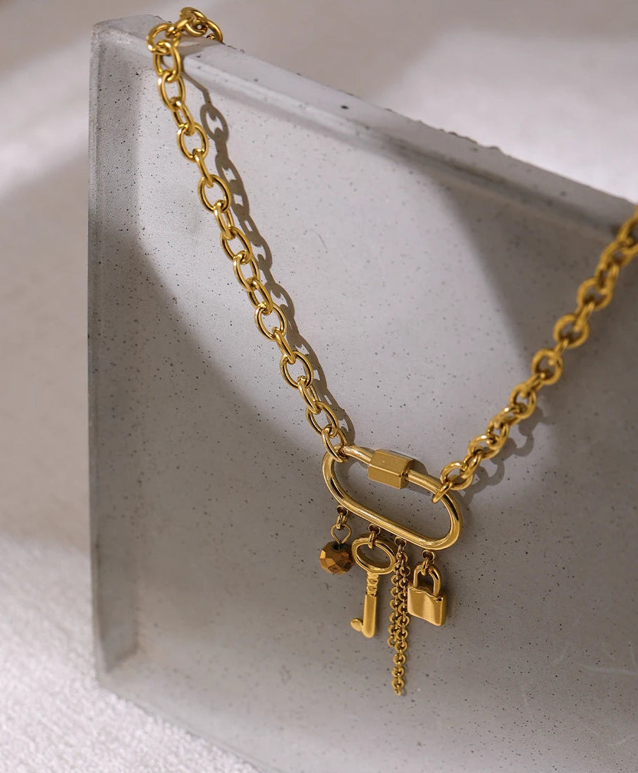 Gold chain necklace with lock and key charms on a light gray surface