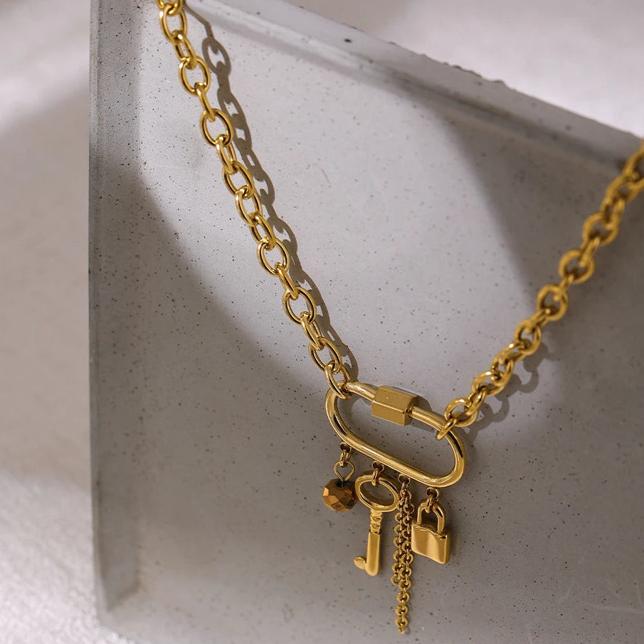 Gold chain necklace with lock and key charms on a light gray surface