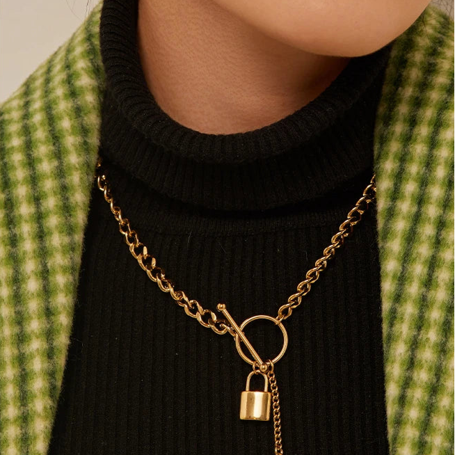 Gold necklace with lock and key pendant worn by a person in a green checkered jacket.