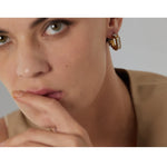 Close-up of a person wearing gold hoop earrings with a neutral background
