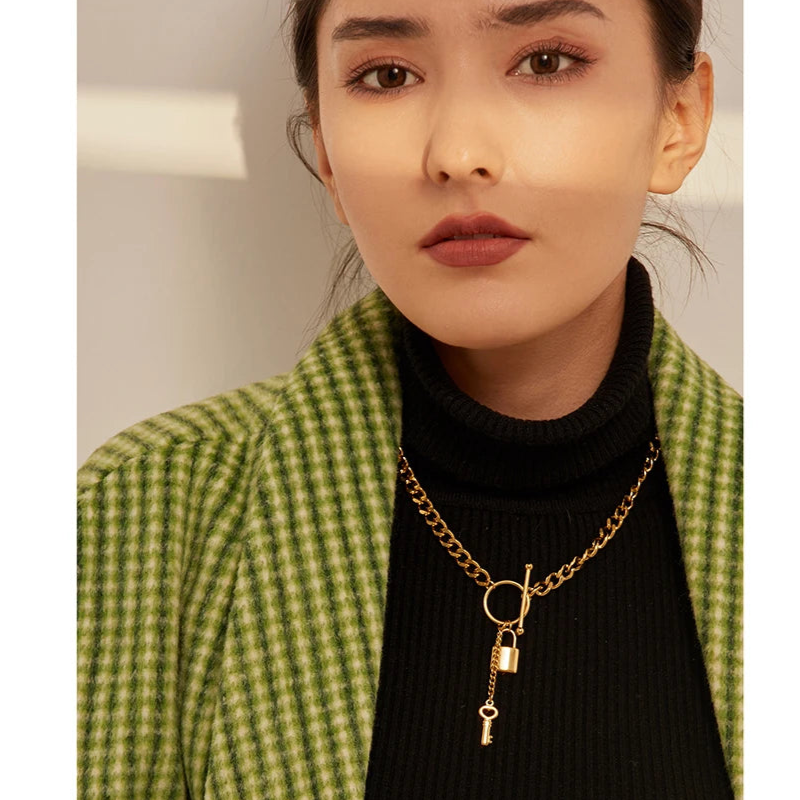 Woman wearing a green checkered coat and black turtleneck with a gold necklace featuring a key pendant.