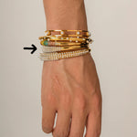 Hand wearing multiple gold and pearl bracelets on a neutral background

