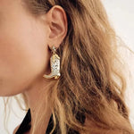 Close-up of a person wearing a gold earring shaped like a cowboy boot with a star on an ear.