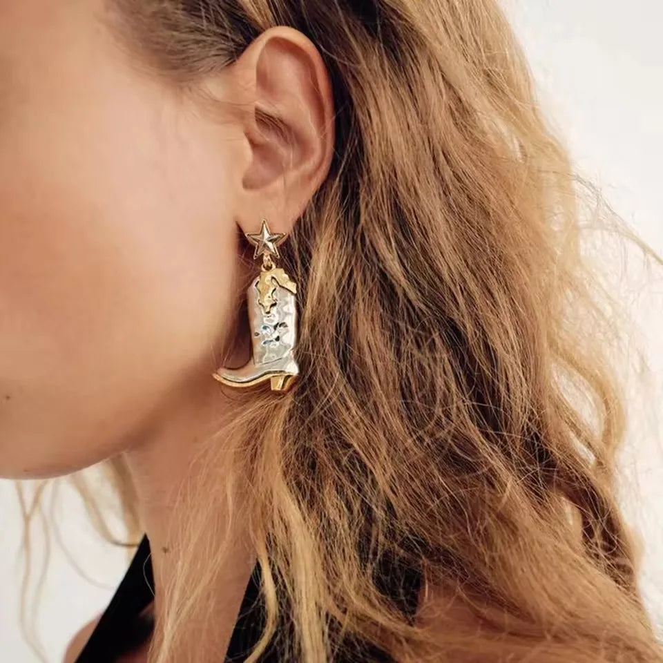 Close-up of a person wearing a gold earring shaped like a cowboy boot with a star on an ear.