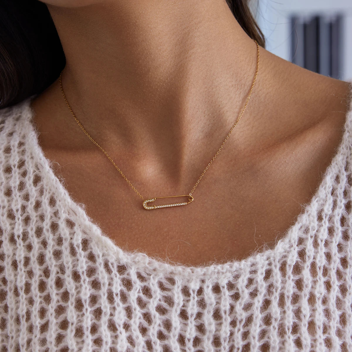 Gold necklace with a bar pendant worn by a person in a white lace top.