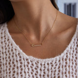 Gold necklace with a bar pendant worn by a person in a white lace top.