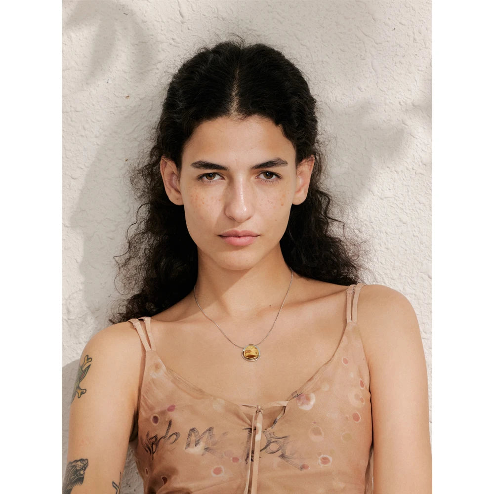 Woman with long dark hair and tattoos on her arms wearing a sheer top against a textured white background