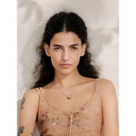Woman with long dark hair and tattoos on her arms wearing a sheer top against a textured white background