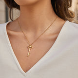 Gold key-shaped necklace on a person wearing a white top