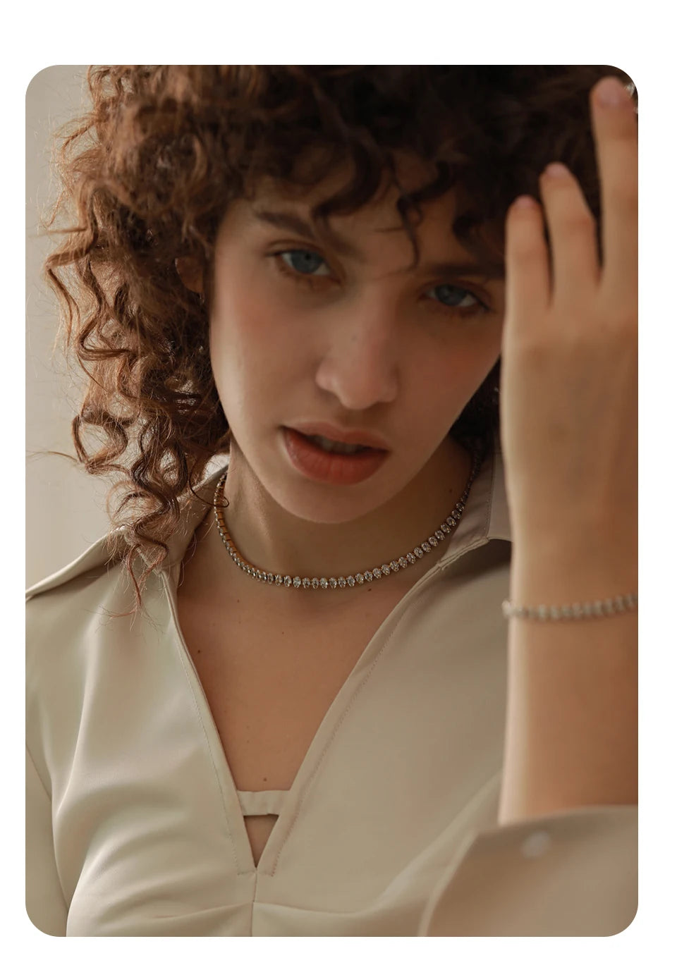 Person with curly hair adjusting their hair, wearing a necklace and bracelet.