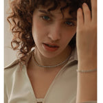 Person with curly hair adjusting their hair, wearing a necklace and bracelet.