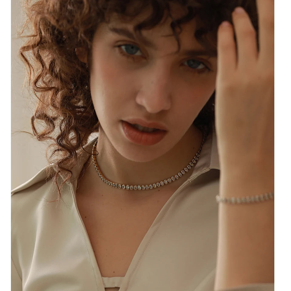 Person with curly hair adjusting their hair, wearing a necklace and bracelet.